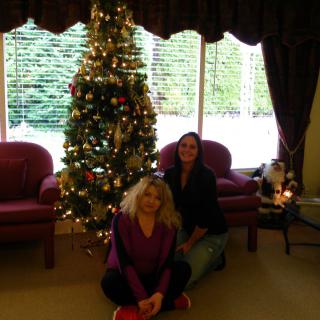 Two people sitting by a decorated Christmas tree in a cozy living room.