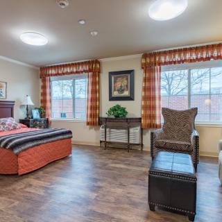 A well-lit bedroom interior featuring a bed, armchair, and wooden flooring.