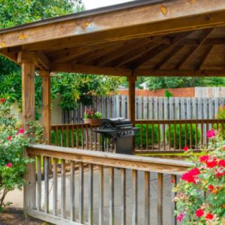 A wooden gazebo in a garden with vibrant roses and a grill.