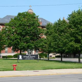 A view of a building surrounded by trees with a sign in front, visible from across the street.
