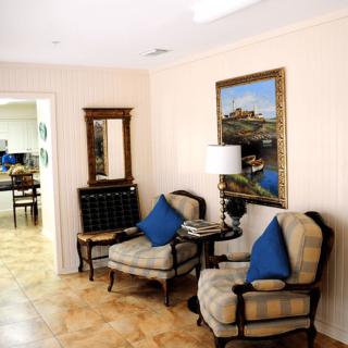 A cozy living room corner with two upholstered chairs, a side table with a lamp, and artwork on the wall.