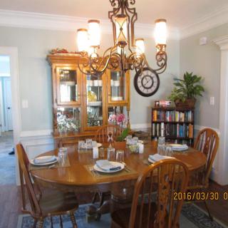 A cozy dining room with a wooden table set for four, surrounded by chairs, a chandelier overhead, and a china cabinet in the background.