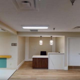 A modern office reception area featuring a central desk with pendant lighting and wooden flooring.