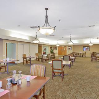A spacious dining room with neatly arranged tables and chairs, featuring elegant chandeliers hanging from the ceiling.
