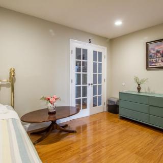 A tidy bedroom with a bed, dresser, small table, and French doors leading to another room.