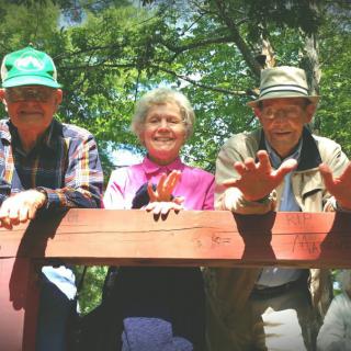 Three seniors enjoying a day outdoors on a wooden platform.