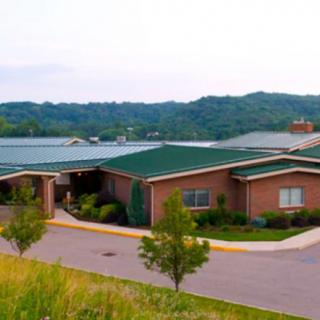A scenic view of a brick building with a green roof, surrounded by trees and hills.