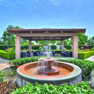 A beautiful garden with a central fountain and a shaded pergola surrounded by lush greenery.