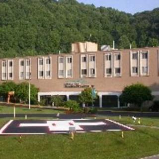 A hospital building with a helipad in front, set against a backdrop of wooded hills.