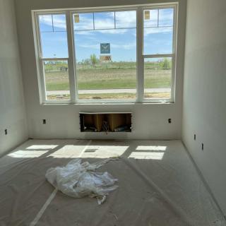 An unfinished room with a large window and floor covering, under construction.
