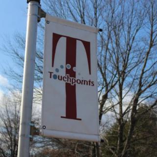 A vertical sign with a logo and text reading 'Touchpoints' against a backdrop of trees and sky.