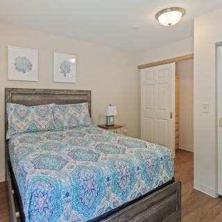 A cozy bedroom featuring a neatly made bed with decorative bedding, artwork on the walls, and a bedside lamp.