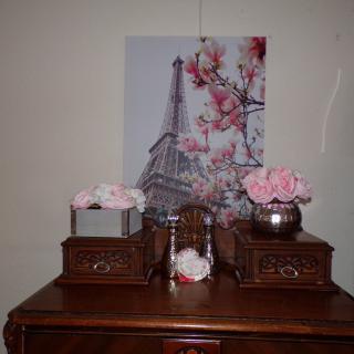 A beautifully decorated wooden dresser with floral arrangements and a painting of the Eiffel Tower.