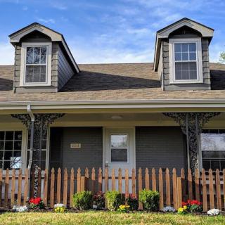 A quaint house with two dormer windows, a wooden fence, and a small garden of flowers in the front yard.