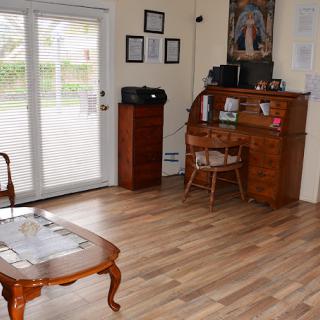 A cozy living room with wooden flooring, featuring a classic wooden desk and chair, a coffee table, and a sliding glass door letting in natural light.