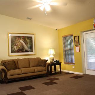 A cozy living room featuring a sofa, artwork on the wall, and a warm lamp beside a window.
