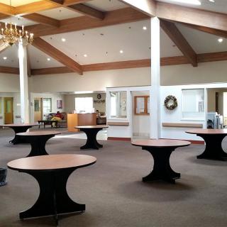 Spacious banquet hall with round tables, a chandelier, and exposed ceiling beams.