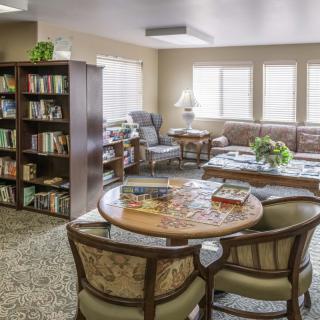 A cozy library room with bookshelves, a seating area, and a round table surrounded by chairs.