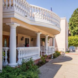 A residential building with a grand porch featuring columns and balustrades, alongside a driveway and surrounded by greenery.