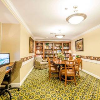 A cozy library and meeting area featuring bookshelves, a large table, comfortable seating, and a computer workstation.