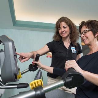 A trainer assists a woman during her workout on a treadmill.