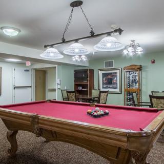 A cozy game room featuring a red-felt pool table under elegant lighting.