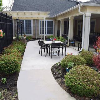 A serene patio setup with a pathway leading to outdoor furniture surrounded by lush landscaping.