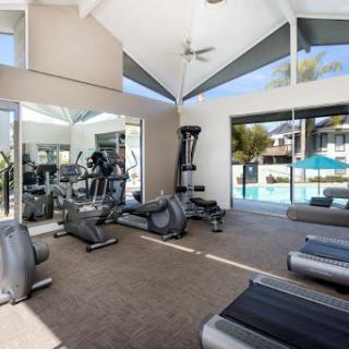 A bright and airy fitness room with modern exercise equipment, featuring large windows that offer a view of the pool.