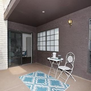 A cozy patio features a small table with two chairs, a decorative rug, and is enclosed by large windows and a sliding glass door.