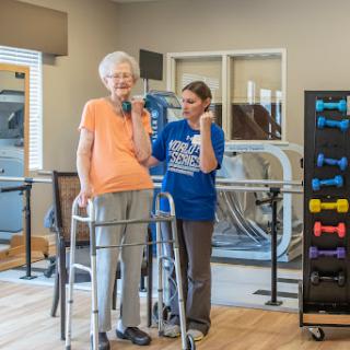 An elderly woman receiving support during a rehabilitation exercise session.