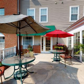 A cozy patio area with tables and chairs under colorful umbrellas, set against the backdrop of a building exterior.