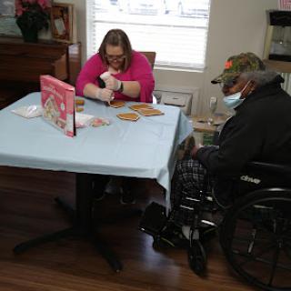 A caregiver engages in a craft activity with an elderly individual in a wheelchair, fostering connection and creativity.