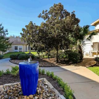 A beautifully landscaped garden with a striking blue fountain and winding pathways under a clear, sunny sky.