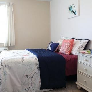 A cozy bedroom with a neatly made bed, colorful pillows, and a nightstand by the window.