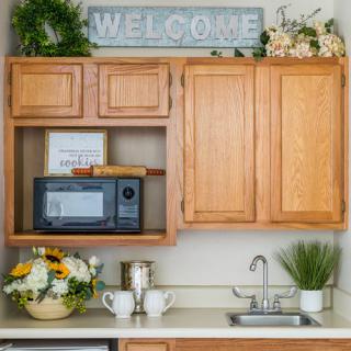 A cozy kitchen nook featuring wooden cabinets, a microwave, floral decorations, and a welcoming atmosphere.
