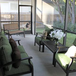 A cozy screened porch with green-cushioned furniture and a view of the backyard.