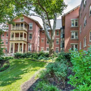 A beautiful brick apartment building surrounded by lush greenery and a garden.