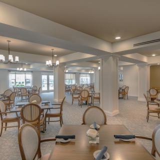 A spacious dining room with elegantly arranged tables and chairs, illuminated by chandeliers.