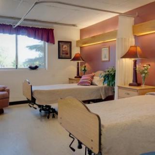 A hospital room with two beds, warmly decorated and well-lit by natural light from a window.