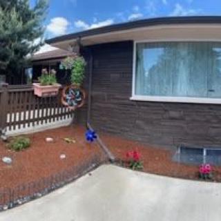 A house with a small garden featuring hanging plants and a flower pot, adjacent to a driveway.