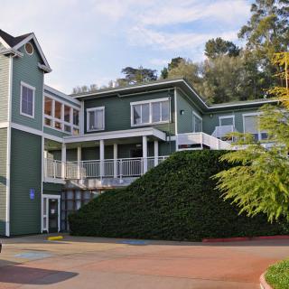 A large green residential house surrounded by trees on a sunny day.