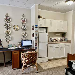A cozy office space with a desk and computer, connected to a small kitchenette adorned with decorative plates.