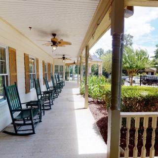 A long porch with a row of rocking chairs and ceiling fans, overlooking a garden.