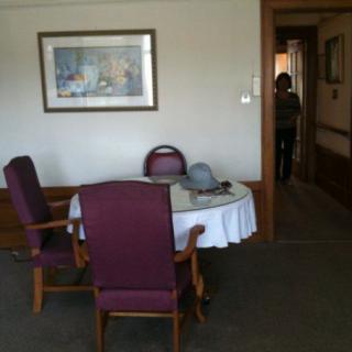 A room with a table and chairs, featuring artwork on the wall and a person standing in the doorway.