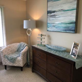 A cozy living room corner with a patterned chair, a modern lamp, and decorative elements on a wooden dresser.