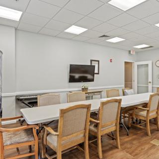 A modern conference room with a long table, office chairs, and a wall-mounted television.