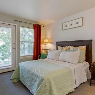 A cozy bedroom with a neatly made bed and natural light coming through the windows.