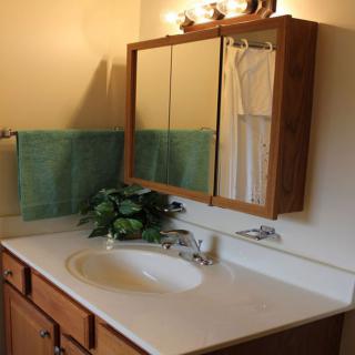 A bathroom featuring a sink with a wooden vanity, a mirrored cabinet above, and a towel hung on the wall.