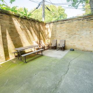 A secluded outdoor seating area with benches and chairs, surrounded by walls and dappled sunlight.