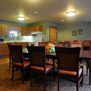 A cozy dining area connected to a kitchen, featuring a large table surrounded by chairs and warm lighting.